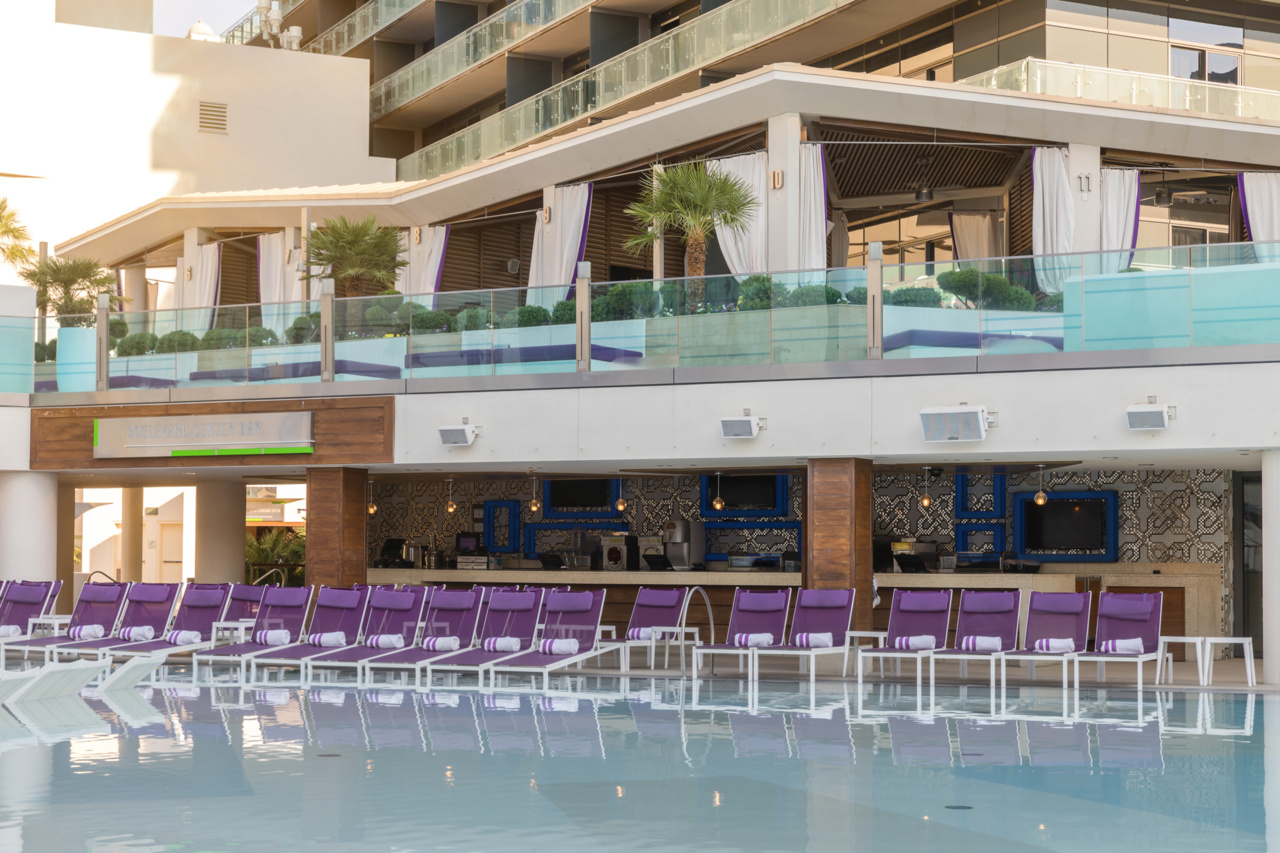 a pool with purple chairs and a building with a balcony