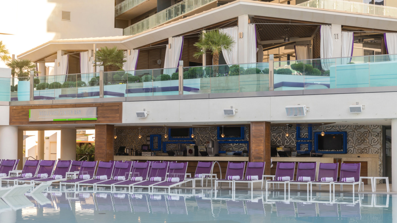 a pool with purple chairs and a building with a balcony