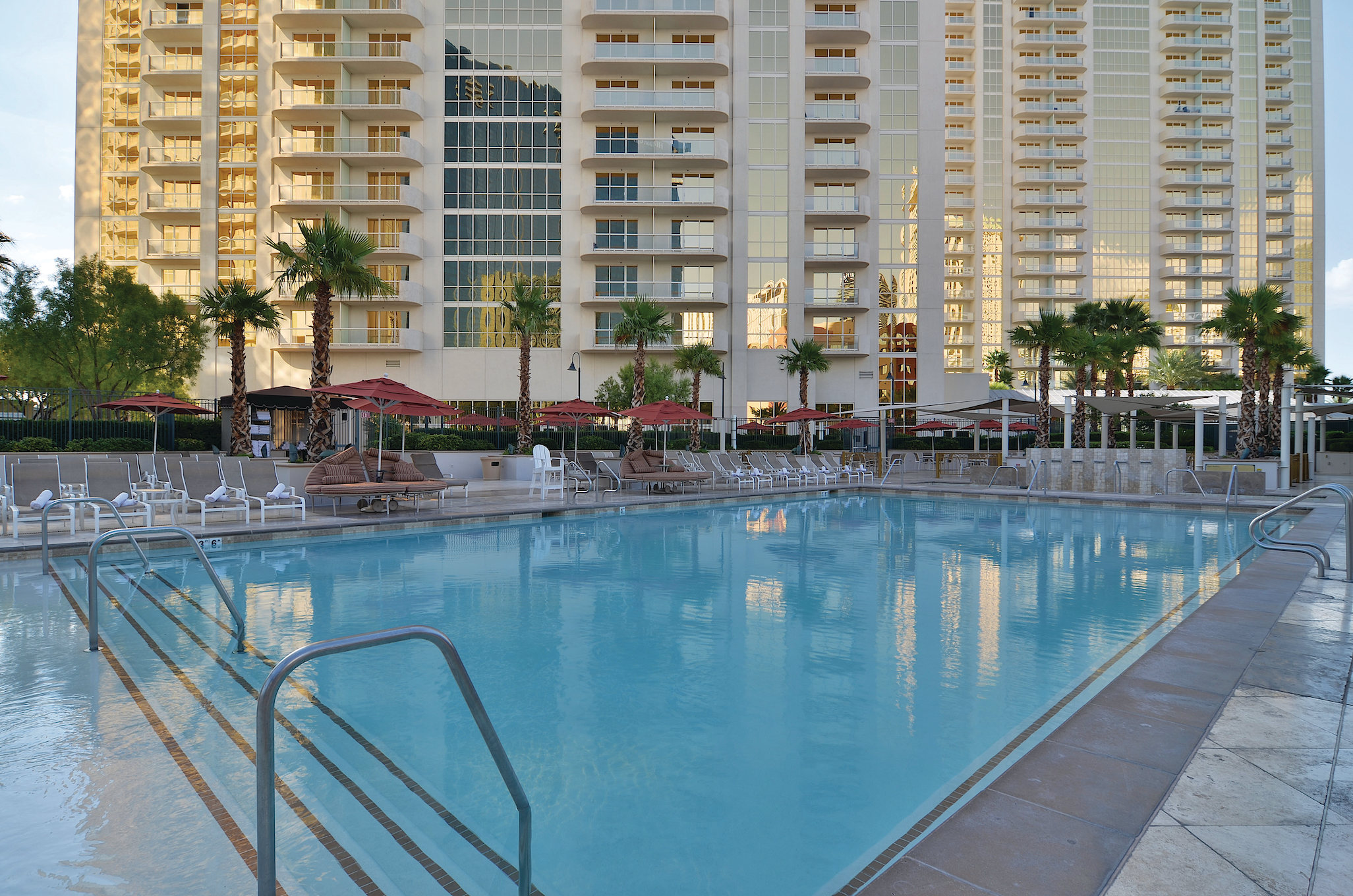 a swimming pool with palm trees and umbrellas in front of a building