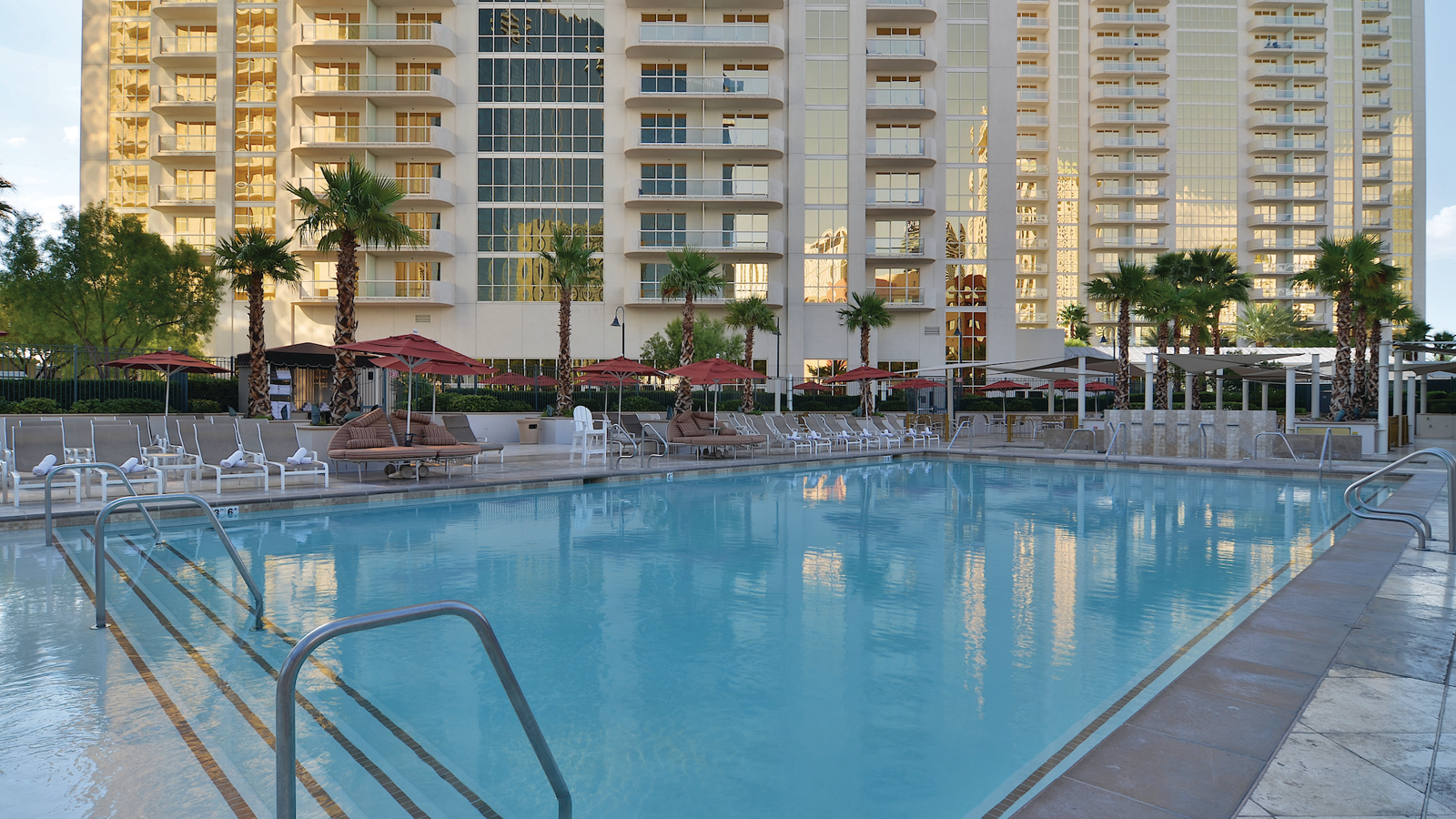 a swimming pool with palm trees and umbrellas in front of a building