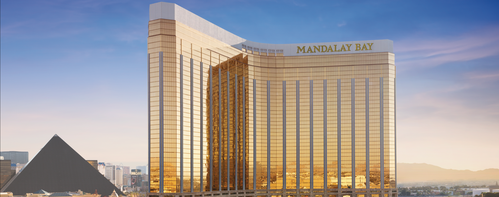 a large gold and white building with palm trees and a pool with Mandalay Bay in the background