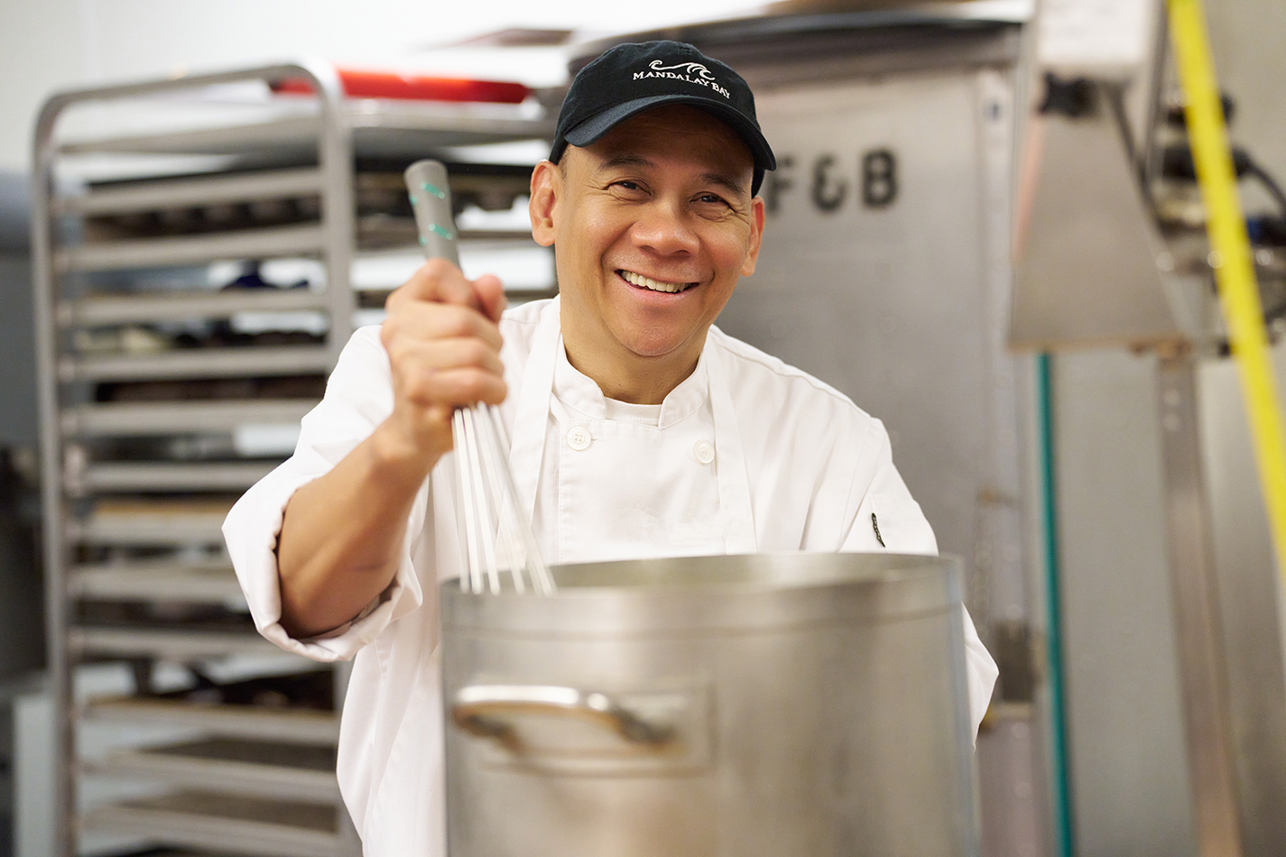 a person in a white coat holding a large pot with whisk