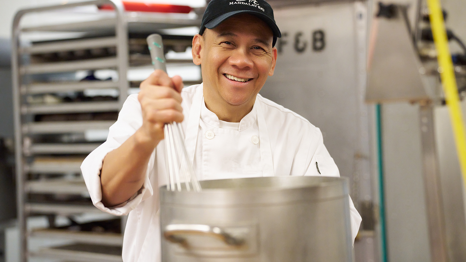 a person in a white coat holding a large pot with whisk